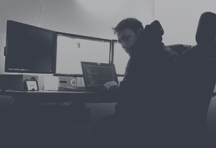 Man sieht mich von schräg hinten links, wie ich gerade mitten in einem Programmierprojekt sitze. Ich schaue über die Schulter in die Kamera.